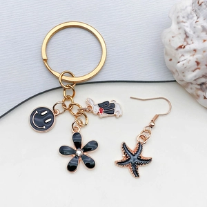 Golden keychain with black enamel smile, flower, and rabbit charms on a shell