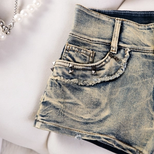 Detailansicht der Used-Denim-Shorts mit Metallnieten und Vintage-Waschung Textur