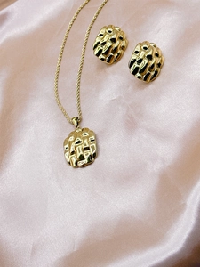 Detail view of gold shell pearl necklace and earring set on pink silk background