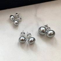 Three pairs of elegant grey pearl stud earrings displayed on a marble surface