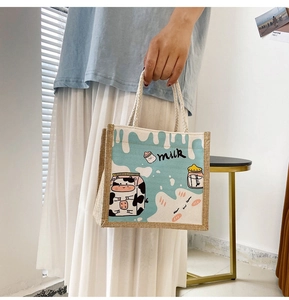 Detail of light blue cartoon cow tote bag with woven rope handles and milk illustration