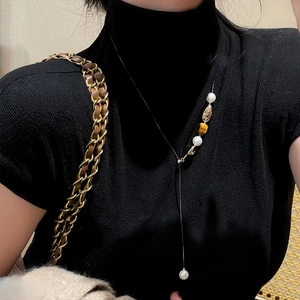 Detail der Tigerauge-Perlenkette getragen über einem schwarzen Rollkragenpullover