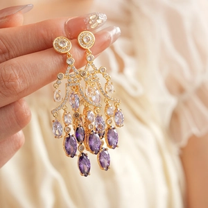 Detailed close-up of golden teardrop earrings with sparkling purple zircon crystals