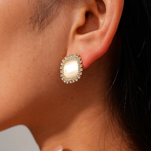 Close-up of vintage gold stud earring with oval cat eye stone and crystal halo on ear