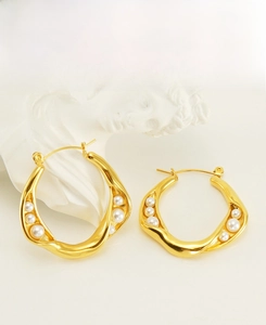 Detail of gold wavy earrings featuring five gradient white pearls in a retro French style
