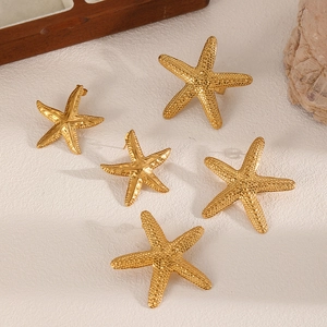 Flat lay of five golden starfish stud earrings on a textured background with sea shell