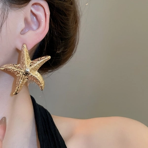 Nahaufnahme eines Models mit großen goldenen Seestern-Ohrringen mit Metallstruktur