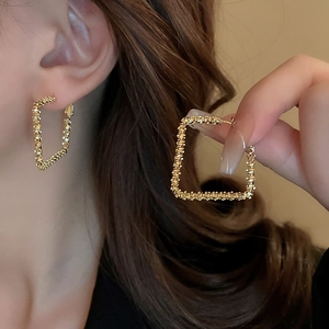 Detail of golden geometric square earrings with textured beaded finish and vintage style