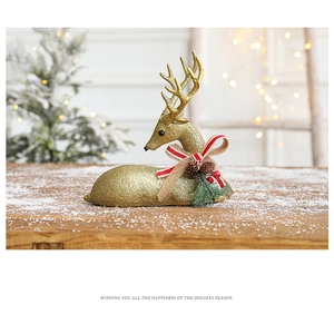 Detail of a gold glitter reindeer figurine with a red bow and pine cones on a snowy wood surface