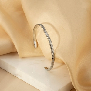 Sleek silver open cuff bracelet with irregular hammered texture on white marble base