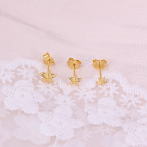 Macro shot of three golden star-shaped earrings on lace background showing fine metal details