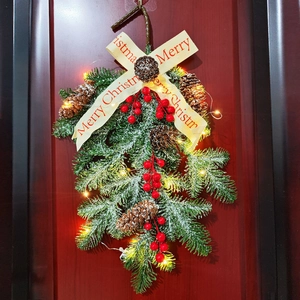 Frosted Christmas wreath with pine cones, red berries, and warm LED lights on a wooden door