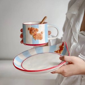 Detail of hand-painted puppy ceramic mug and plate set with blue stripes and red trim