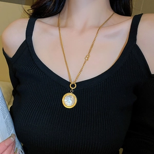 Detail of gold necklace with round white shell pendant and small B letter charm on a model