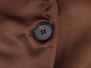 Gros plan d'un bouton noir à quatre trous sur un tissu en satin de soie marron