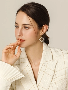 Dettaglio di orecchini geometrici con strass indossati da una modella in abito beige