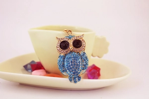 Detail of owl pendant with blue rhinestones resting on a miniature tea cup