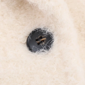 Detail of cream plush fabric texture and black four-hole button on chic women's coat