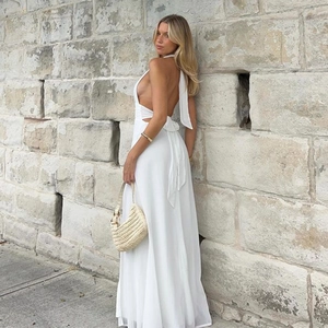 Detail of a white halter backless maxi dress with a side slit and woven bag accessory