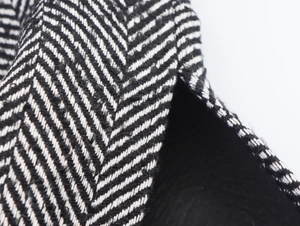 Macro shot of black and white herringbone fabric with leather piping and stitching details