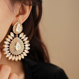 Close-up of teardrop-shaped gold stud earring with sparkling champagne crystals on model