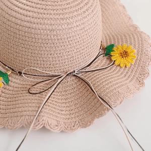 Dettaglio cappello di paglia con tesa ondulata, ricamo a girasole e fiocco intrecciato