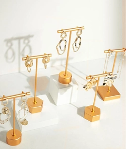 Detail of gold metal earrings with pearls on a T-bar stand over white plaster blocks