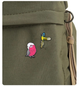 Detailed view of colorful parrot enamel pins attached to an olive green fabric backpack