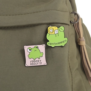 Detail of cute frog enamel pins with puns pinned on an olive green backpack
