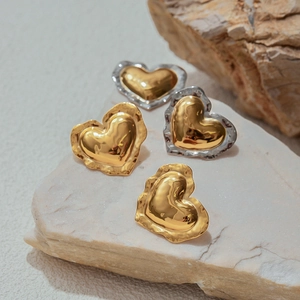 Close-up of irregular heart earrings in gold and silver on a textured stone base