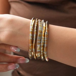 Detail of layered gold and silver mixed-metal snake chain bracelets on a wrist