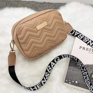 Quilted camera bag with wave stitching and wide jacquard strap on plush background