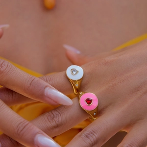 Detail of heart enamel rings in pink and white with gold band on model hand