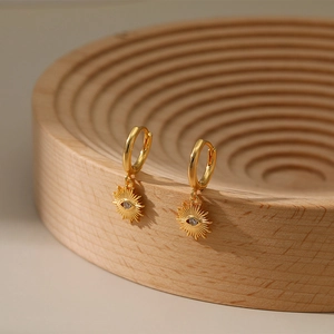 Close-up of gold plated sun-shaped evil eye earrings with zircon on a wooden display