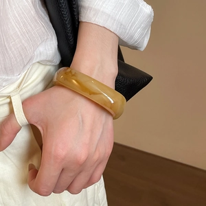 Close-up of thick amber resin bangle showing realistic marbled texture on woman's wrist