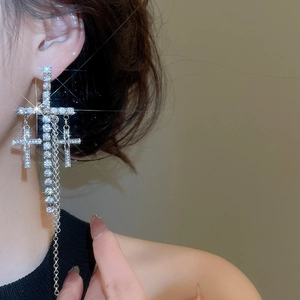 Close-up of model wearing silver cross tassel earrings with sparkling rhinestones