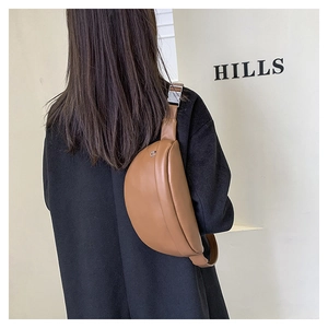 Detail view of brown leather half-moon chest bag on black coat with silver buckle