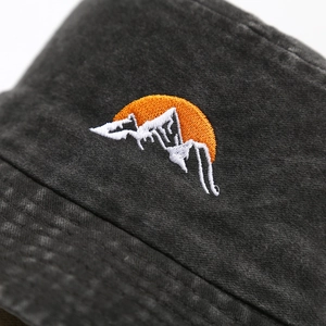 Detail of embroidered mountain sun logo on washed cotton bucket hat with vintage texture
