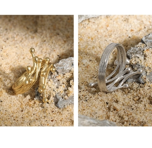 Close-up of gold and silver rings with natural coral branch texture on a sand background