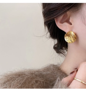 Close-up view of a gold-plated wrinkled round stud earring worn on a model's ear