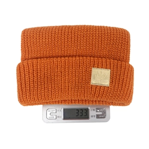 Macro shot of an orange knitted beanie featuring a leather smiley face patch and ribbed texture