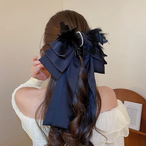 Detail of black ribbon bow hair claw with elegant feathers and pearls on long hair