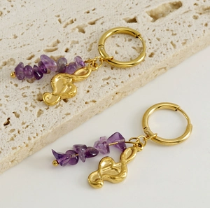 Macro detail of 18k gold earrings with purple natural stone beads and musical note charm
