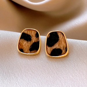 Macro shot of gold-framed leopard print earrings with velvet texture on silk fabric
