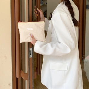 Close-up of cream-colored cosmetic bag held by model, featuring pink contrast zipper