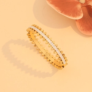 Golden hollow bangle with rhinestones and rivet details on a soft orange background