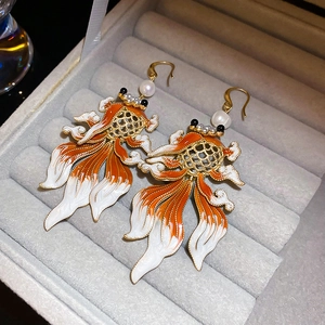 Detailed macro view of goldfish drop earrings with enamel textures and pearl accents