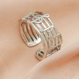 Detail of silver musical note ring with small crystals on a soft satin background