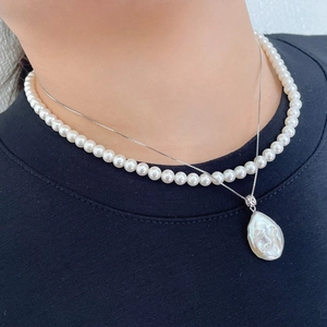 Close-up of layered necklace featuring small white pearls and a baroque pearl pendant