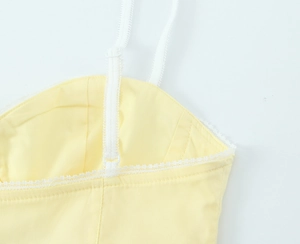 Dettaglio ravvicinato di un top in popeline giallo tenue con pizzo bianco e spalline